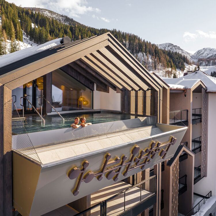 Moderne Hotelarchitektur mit einem Poolbereich, umgeben von alpiner Landschaft und einem einladenden Gästeerlebnis.