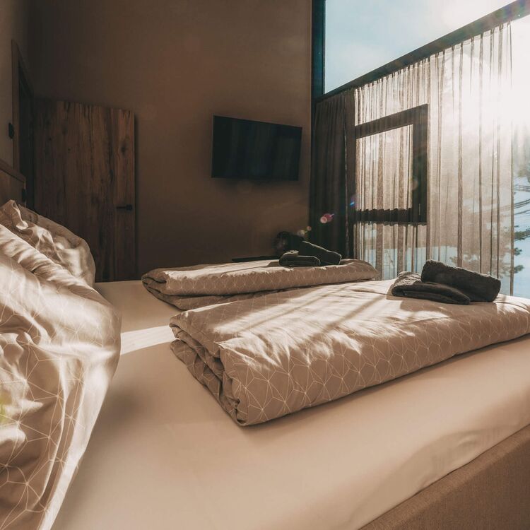 Gemütliches Hotelzimmer mit modernen Akzenten und Blick auf alpine Architektur im Hintergrund.