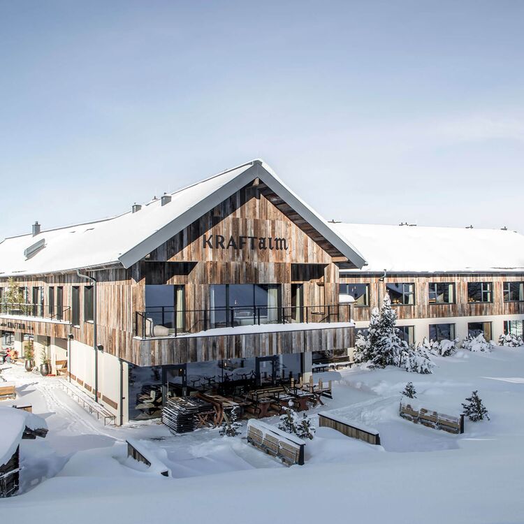 Das stilvolle Hotel Kraftalm zeigt moderne Hotelarchitektur, umgeben von schneebedeckten Alpenlandschaften.