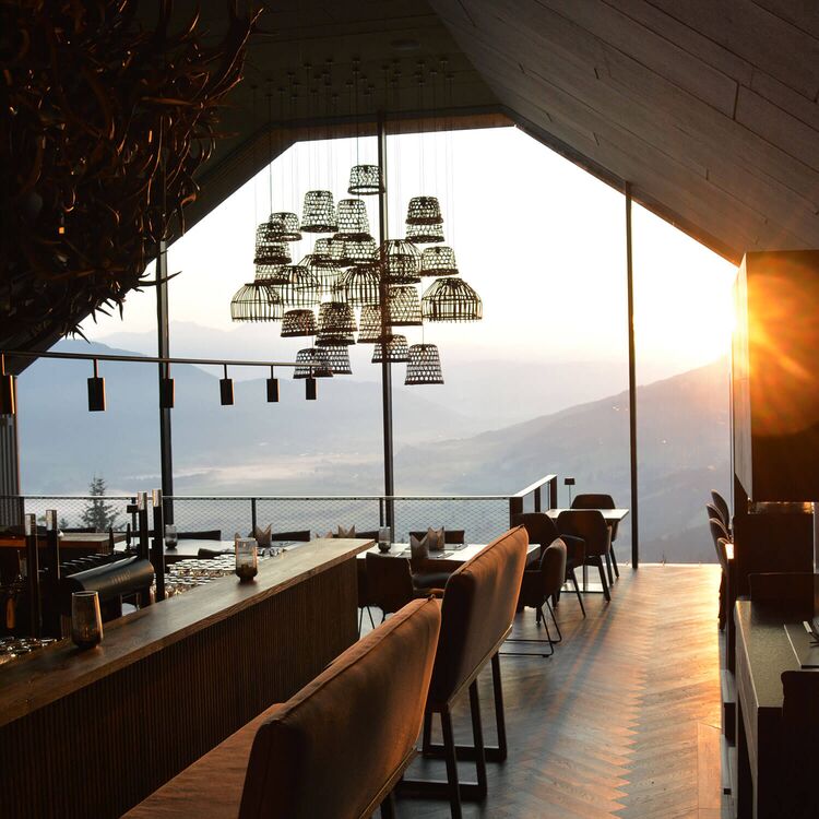 Ein elegantes Restaurant mit Hotelarchitektur, großen Fenstern und stimmungsvollem Lichtblick auf die Alpen.
