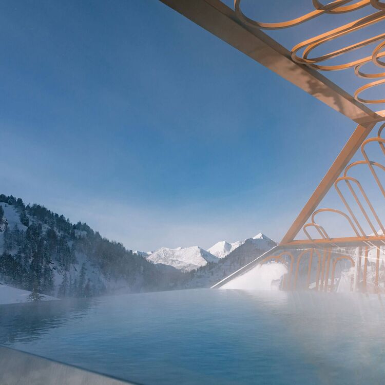 Ein modernes Hotel mit alpiner Architektur bietet einen atemberaubenden Ausblick auf schneebedeckte Berge und einen Pool.