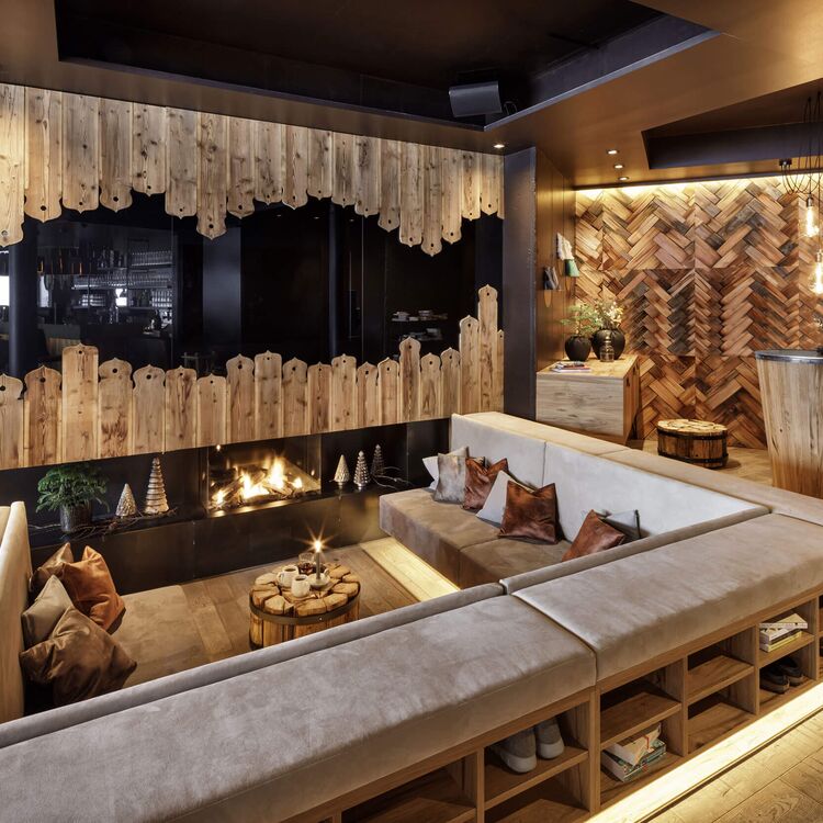 Gemütliche Lounge mit Kamin, modernem Hoteldesign und warmer Holzgestaltung für ein einladendes Gästeerlebnis.