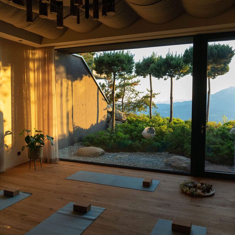 Ein lichtdurchfluteter Raum mit Yoga-Matten und Blick auf alpine Landschaft, ideal für Gästeerlebnisse im Hotel.