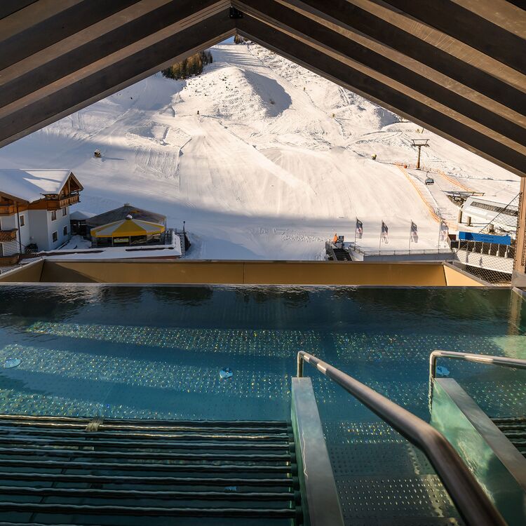 Der Blick von einem modernen Hotelpool auf die verschneiten Pisten zeigt beeindruckende alpine Architektur und Gästeerlebnis.