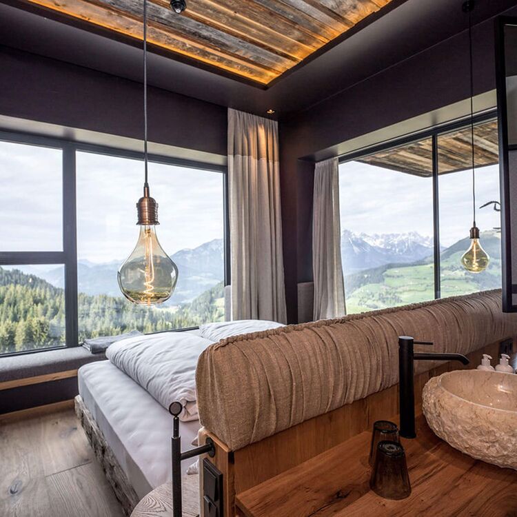 Modernes Hotelzimmer mit alpiner Architektur und großem Fenster, das einen atemberaubenden Blick auf die Berge bietet.