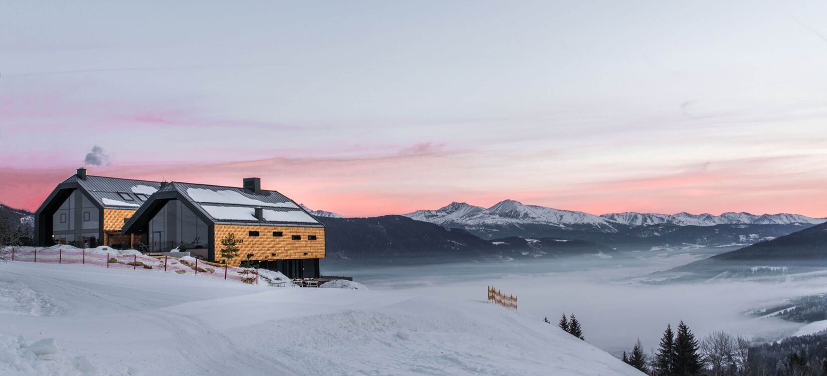Ein modernes Hotel in alpiner Architektur vor einem atemberaubenden Sonnenaufgang über verschneiten Bergen.