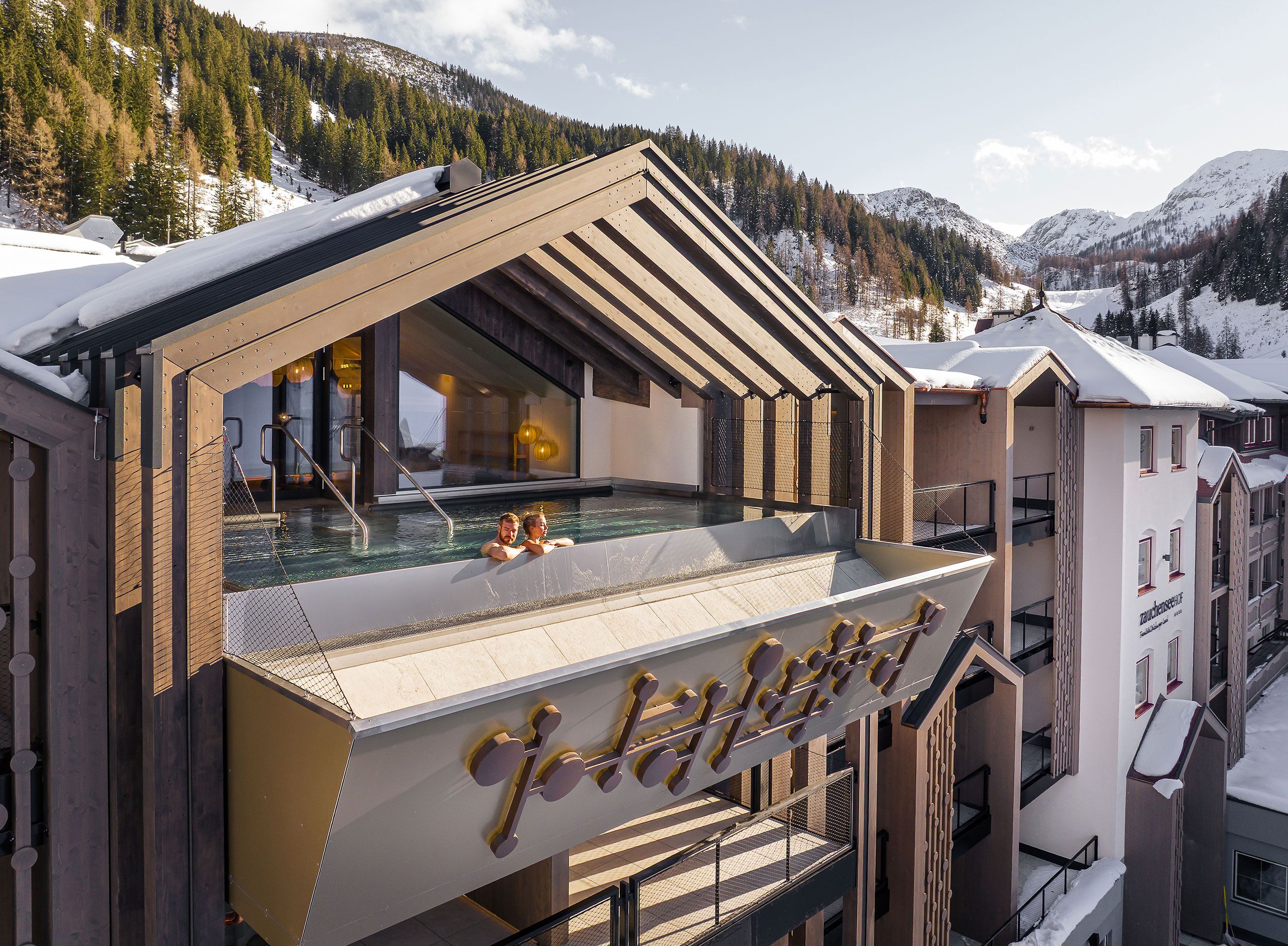 Moderne Hotelarchitektur mit einem Poolbereich, umgeben von alpiner Landschaft und einem einladenden Gästeerlebnis.