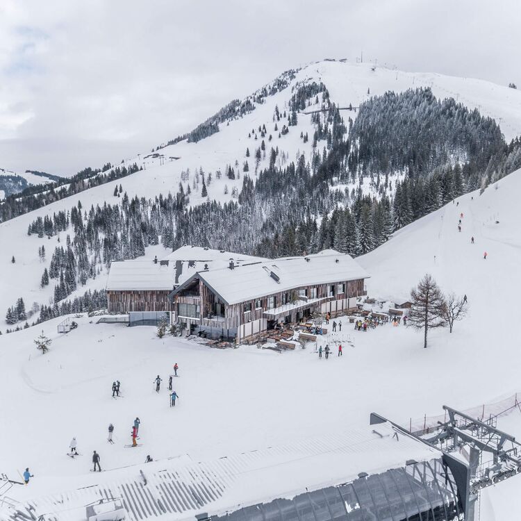 Moderne Hotelarchitektur in alpiner Landschaft mit Skifahrern vor dem Gebäude im Schnee.