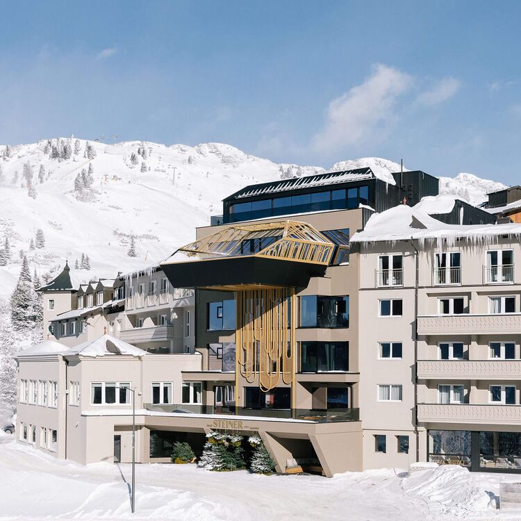 Moderne Hotelarchitektur in den Alpen, umgeben von schneebedeckten Bergen und ideal für ein einzigartiges Gästeerlebnis.