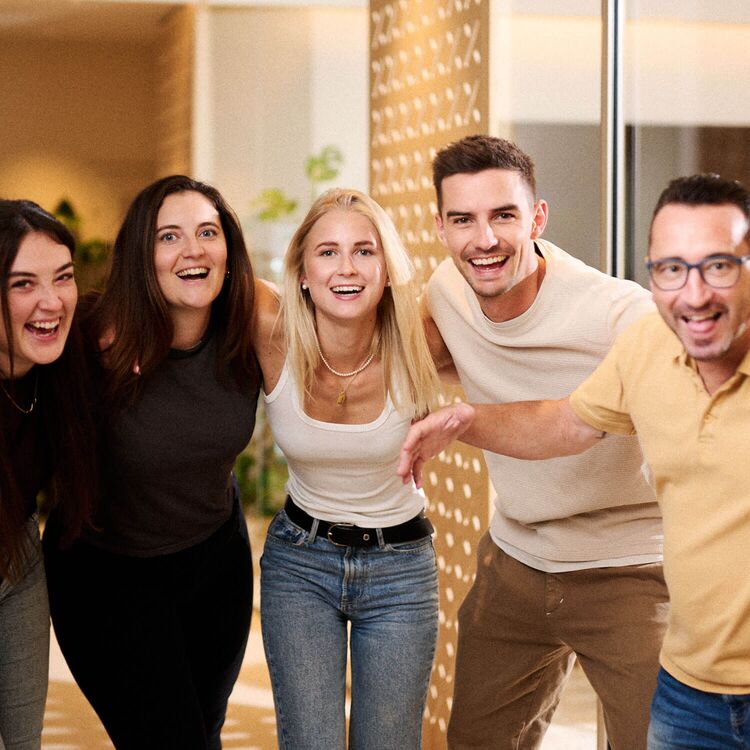 Eine Gruppe fröhlicher Menschen posiert in einem modernen Hotel, das für Gästeerlebnisse und Hotelarchitektur gestaltet ist.